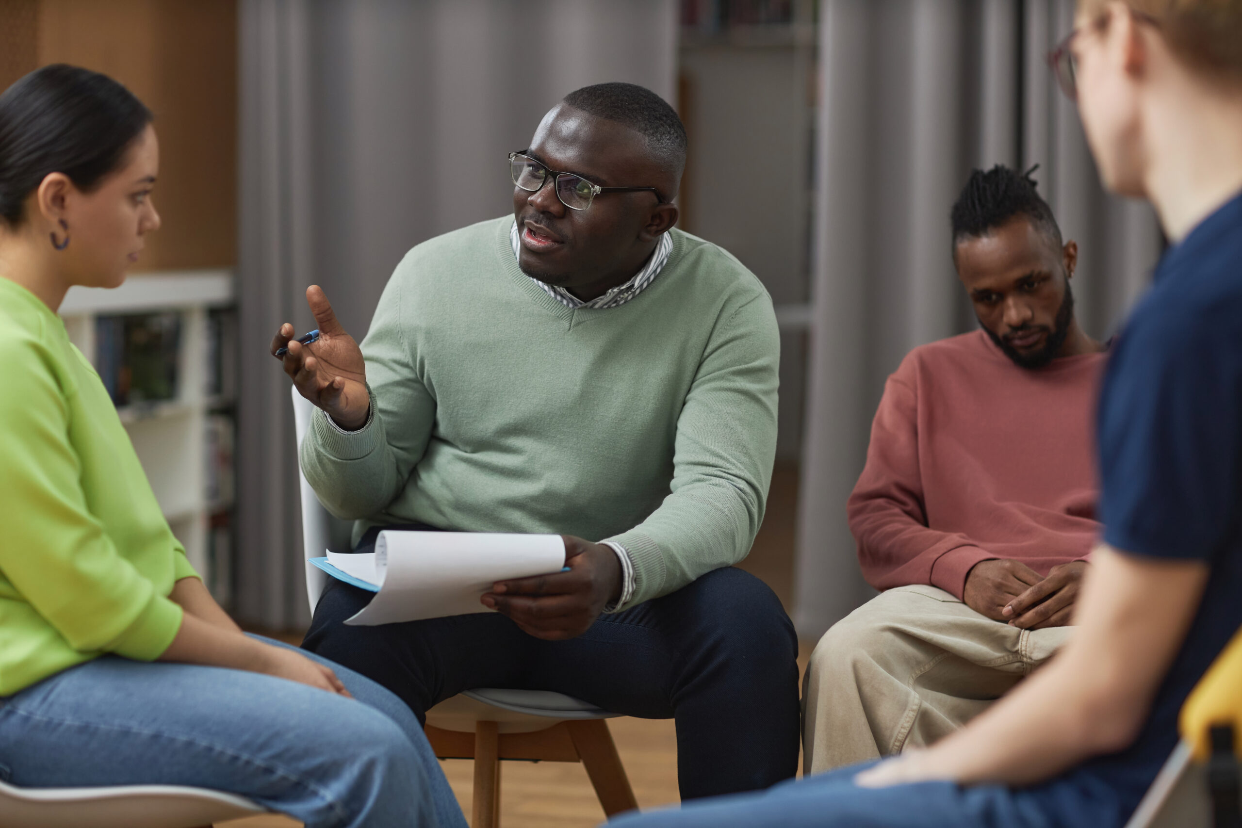 Portrait of black young man as therapist talking to young woman in support group circle